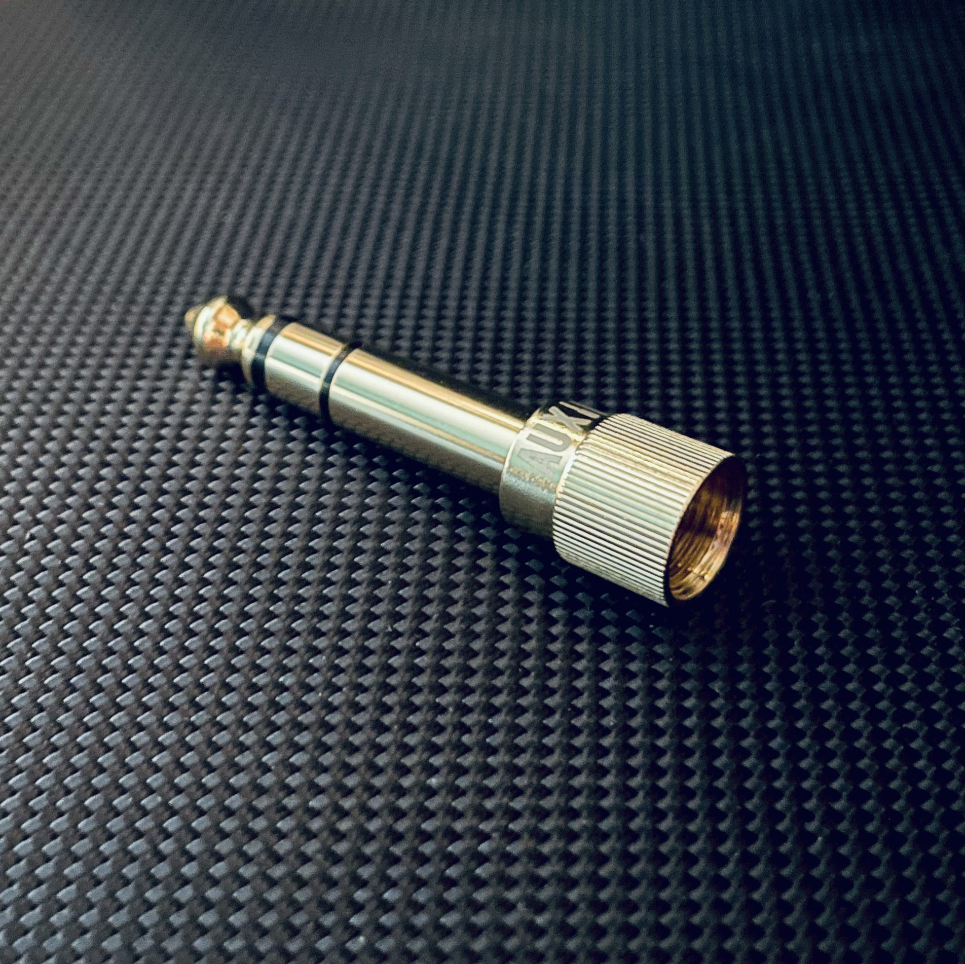 Auxinn gold-plated screw-thread headphone adapter on a dark textured surface